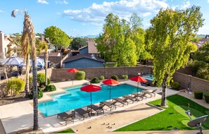 A swimming pool with lounge chairs and umbrellas, surrounded by trees and a brick wall. - Sport Court Pool Hot Tub Pool Table Fire Pit Games (Glendale)