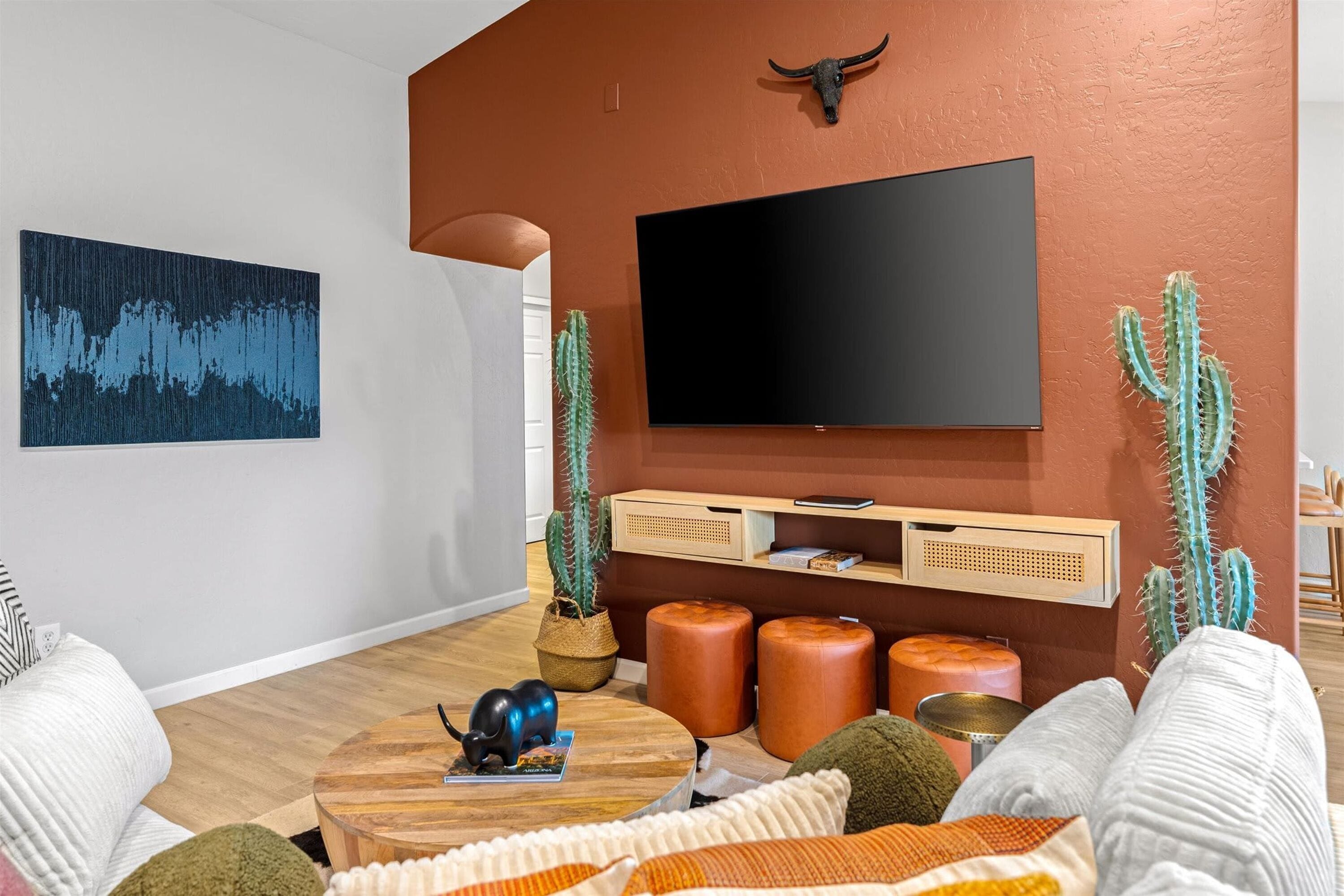 A living room with a flat-screen TV mounted on the wall, a cactus plant, a round wooden coffee table, and a sofa.