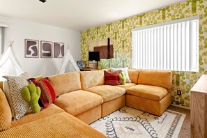 A cozy living room with a sectional sofa, a patterned wall, and a window with blinds. - Sport Court Pool Hot Tub Pool Table Fire Pit Games (Glendale)