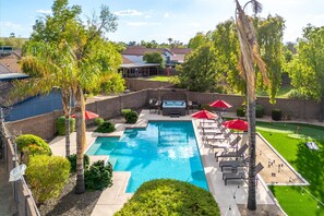 Un patio trasero con piscina, sillas de descanso y un jacuzzi.