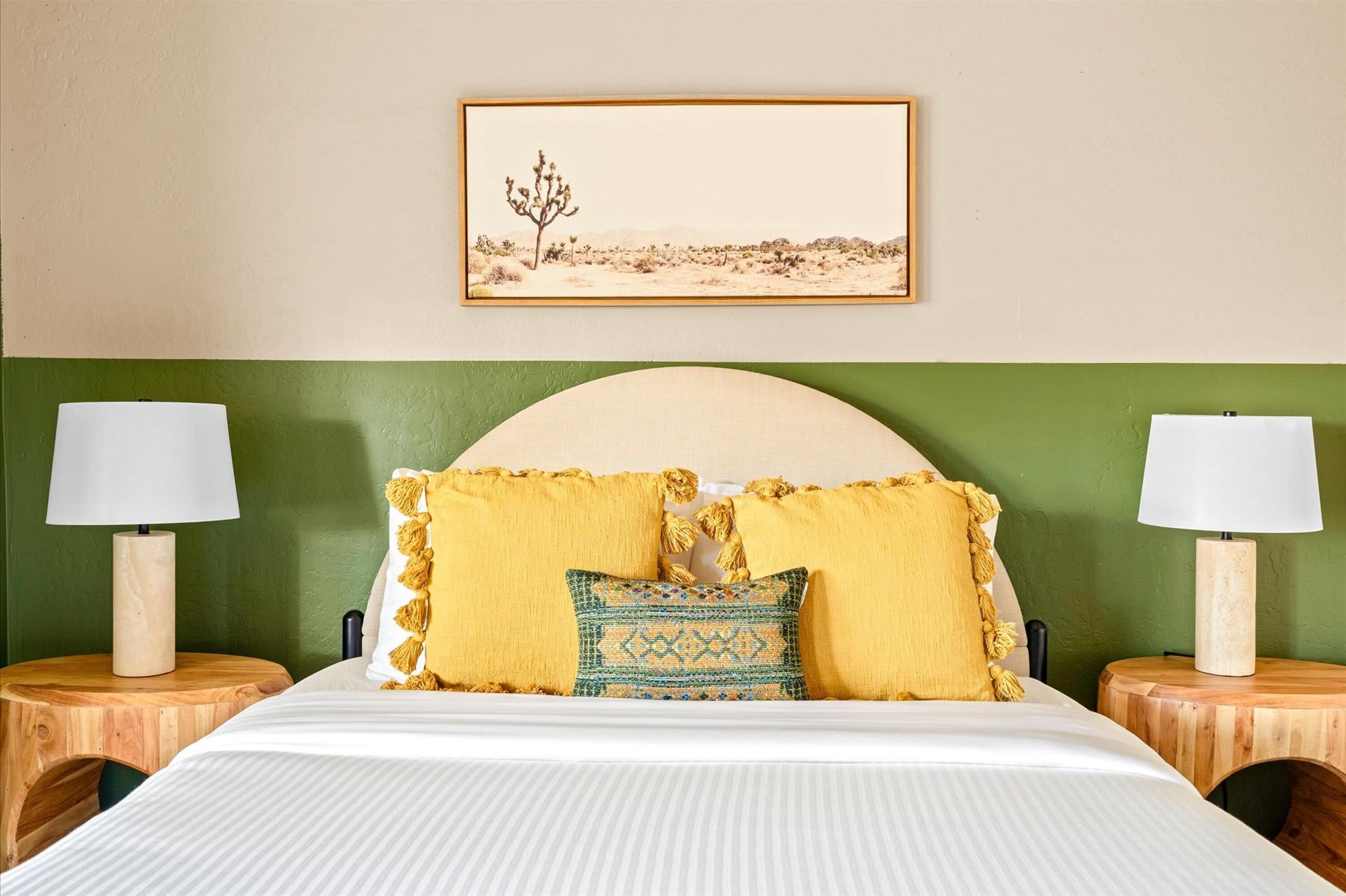 A hotel room with a bed, two nightstands, a lamp on each nightstand, a green wall, a framed picture above the bed, and a headboard.