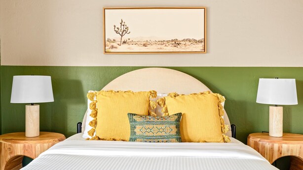 A hotel room with a bed, two nightstands, a lamp on each nightstand, a green wall, a framed picture above the bed, and a headboard. - Sport Court Pool Hot Tub Pool Table Fire Pit Games (Glendale)
