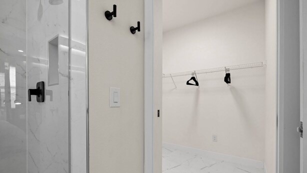 Une salle de bain moderne avec une douche à parois de verre, un sol en marbre blanc et un porte-serviettes avec deux serviettes.