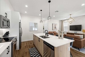 Eine moderne Küche mit Kochinsel, integrierten Geräten und einem Essbereich inklusive Sofa und Fernseher.