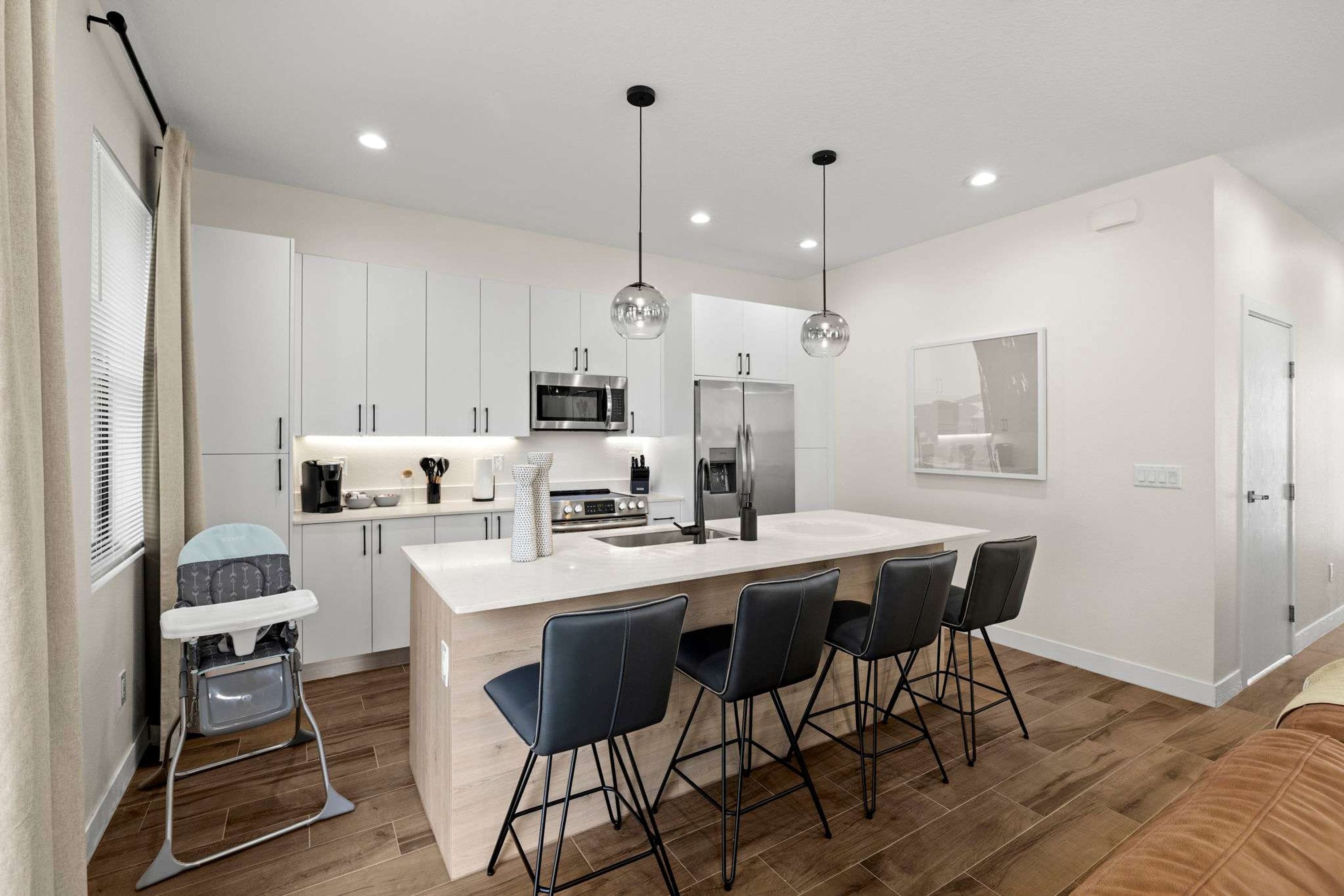 A modern kitchen with white cabinetry, a central island with bar stools, a microwave, a refrigerator, and pendant lighting.