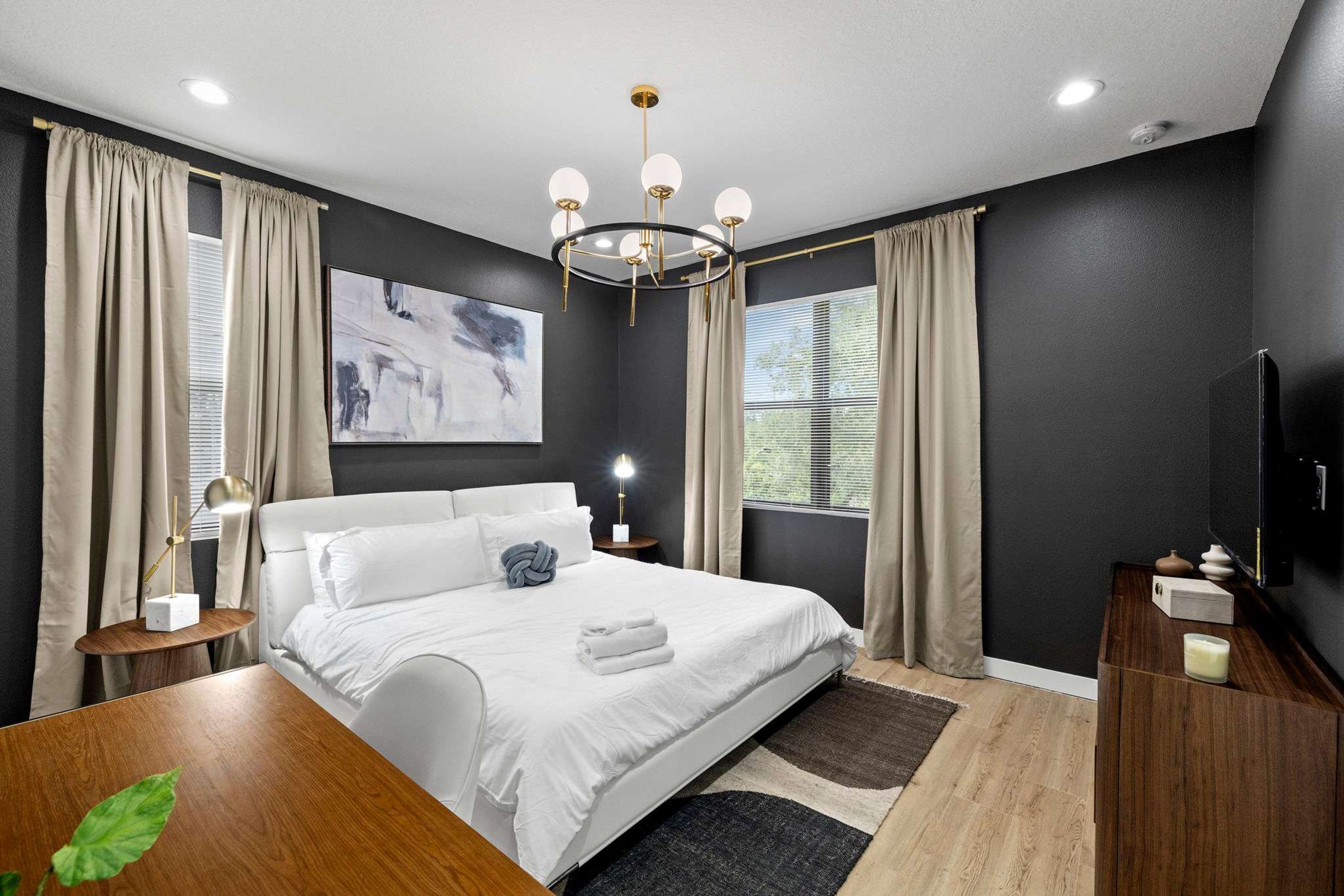 Ein modernes Schlafzimmer mit einem großen Bett, einer Kristallleuchter und einem Gemälde an der Wand.