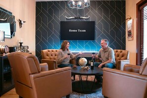 A modern interior with leather sofas, a round coffee table, and a large screen displaying 'Home Team'. - Golden Ridge Lodge - Hot Tub - Games - Mtn Views (Helen)