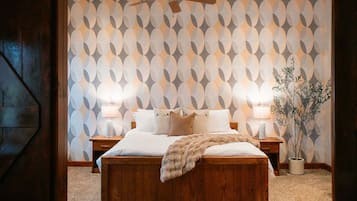 A bedroom with a bed, two bedside tables, a ceiling fan, and a wall with a geometric pattern.
