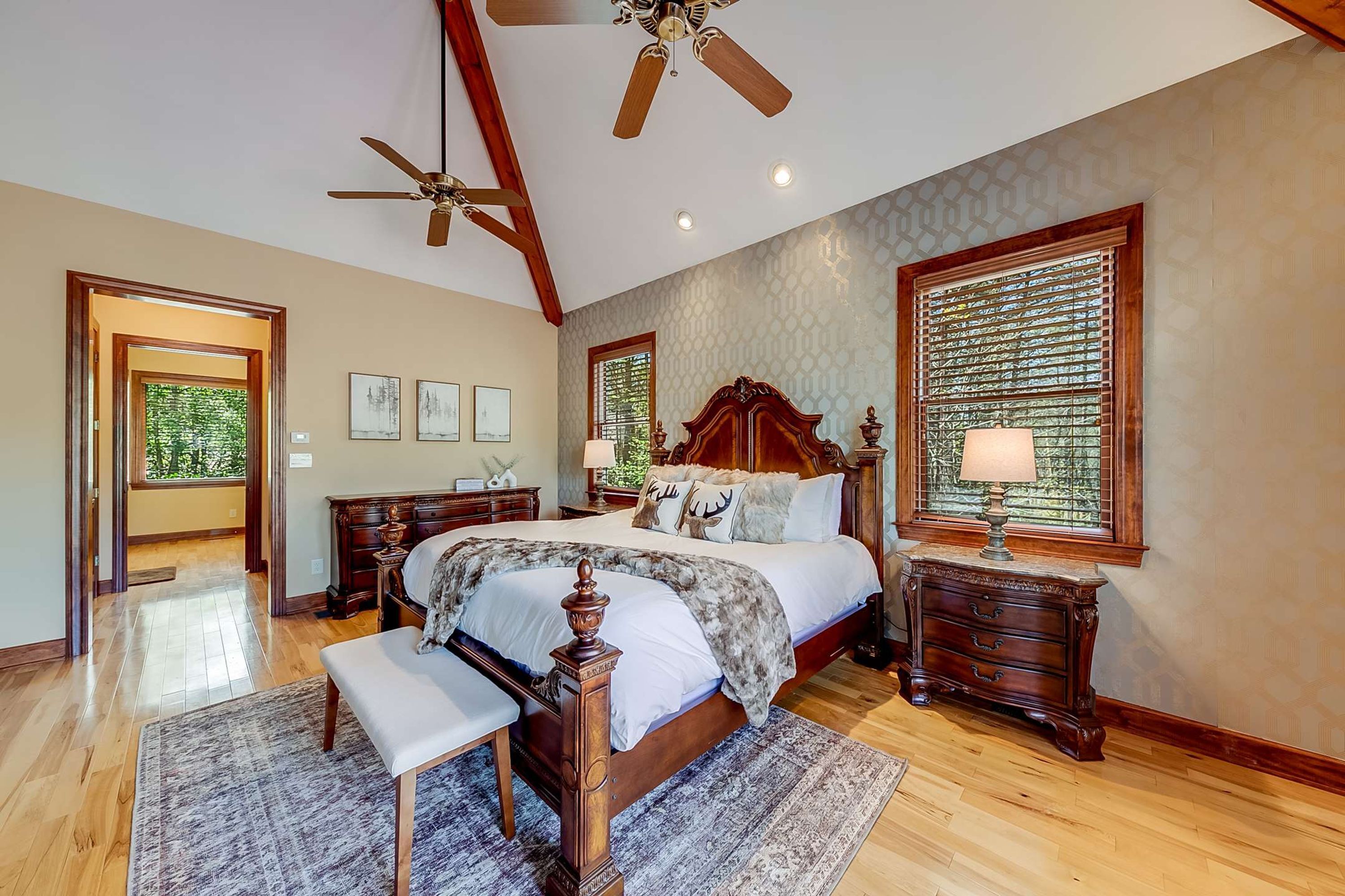 A spacious bedroom with a large bed, wooden headboard, a bench, and a ceiling fan.