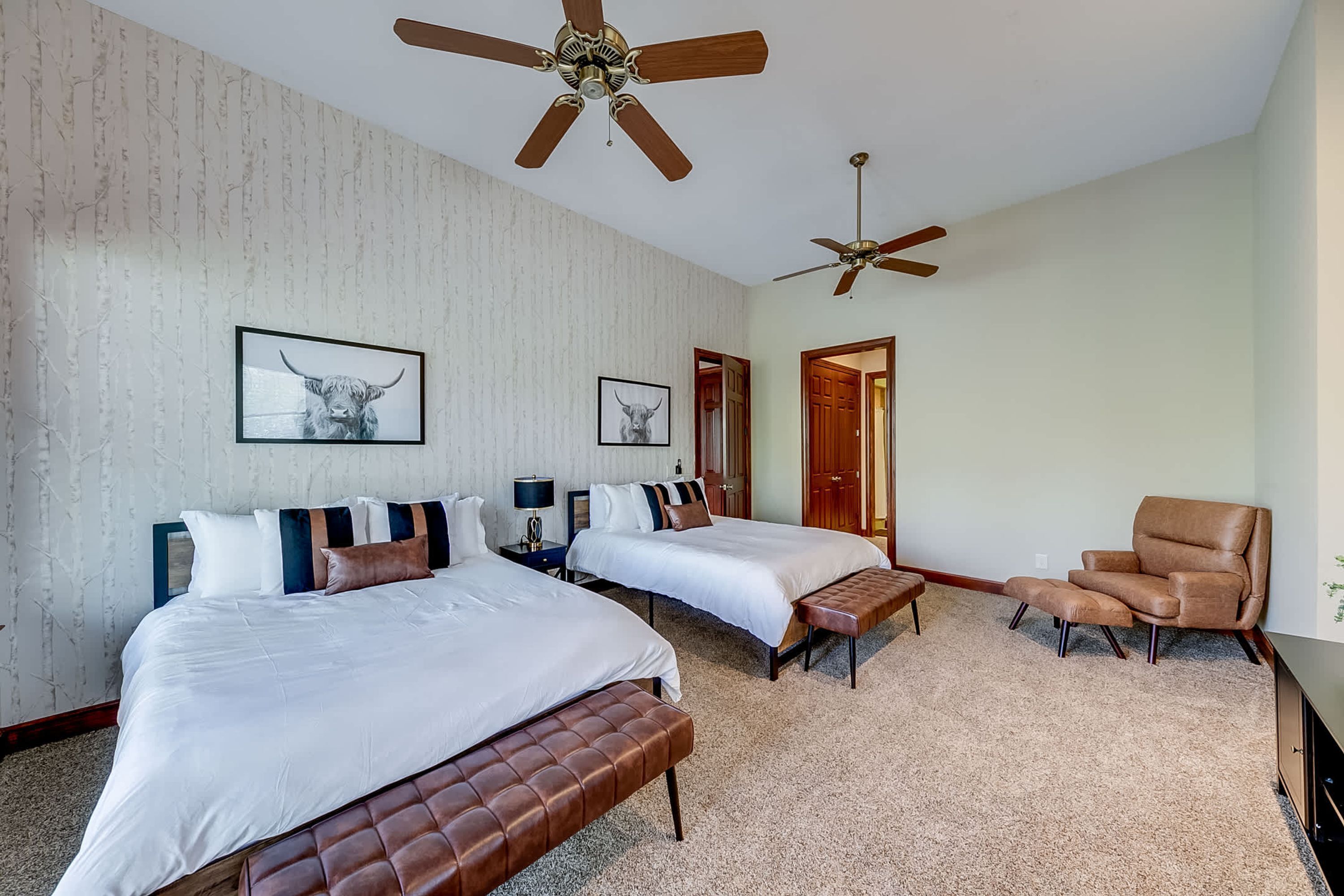A hotel room with two beds, a sofa, a chair, a ceiling fan, and a door leading to another room.