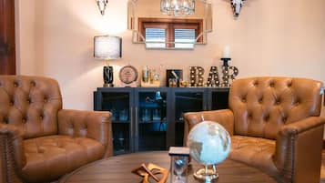 A room with two leather armchairs, a round wooden coffee table, a globe, an hourglass, and a bar sign.