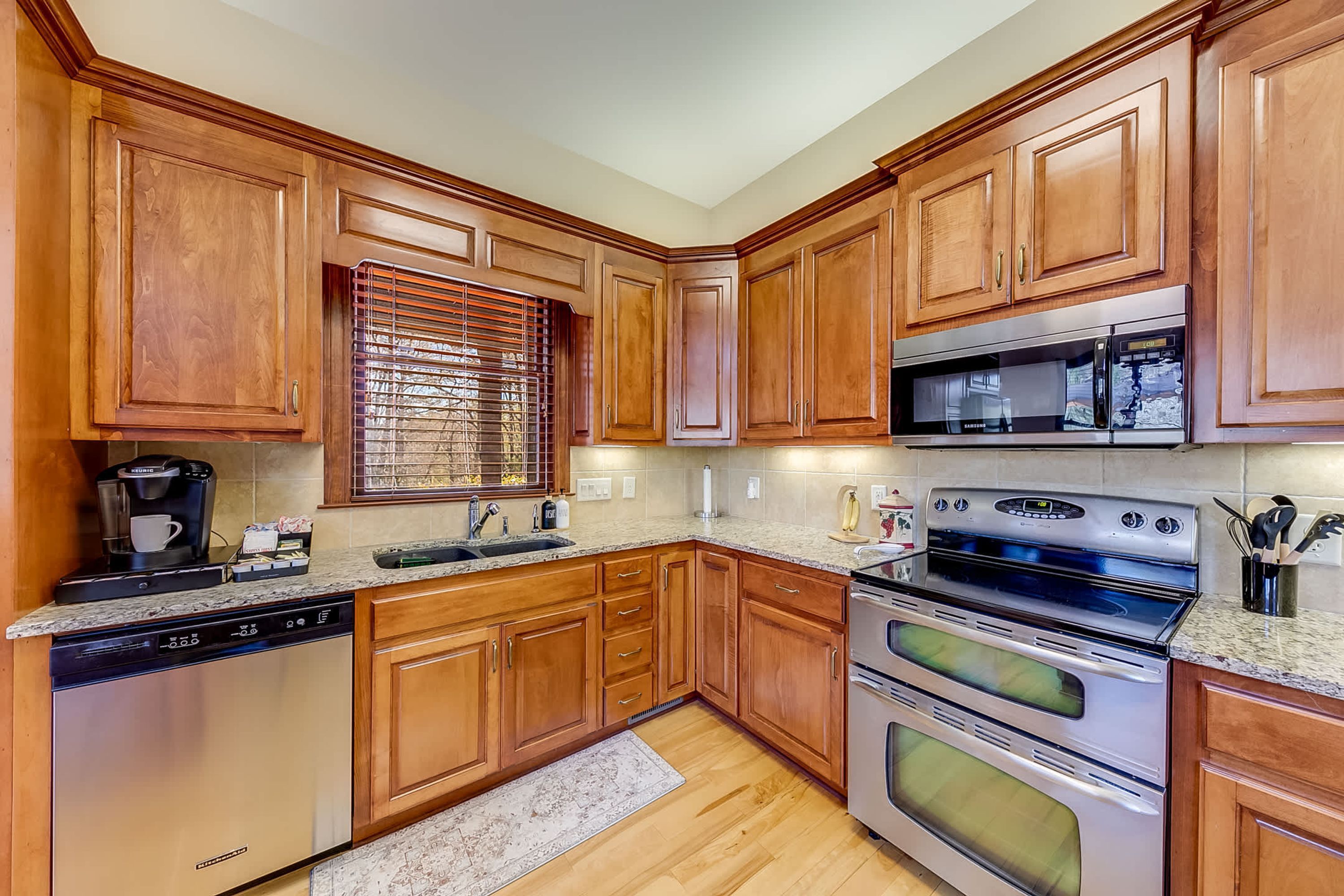 A kitchen with wooden cabinets, stainless steel appliances, a coffee maker, and a window with blinds.