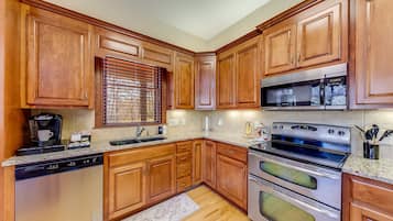 A kitchen with wooden cabinets, stainless steel appliances, a coffee maker, and a window with blinds.