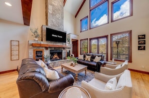 A spacious living room with a stone fireplace, leather sofas, and large windows offering views of the outdoors. - Golden Ridge Lodge - Hot Tub - Games - Mtn Views (Helen)