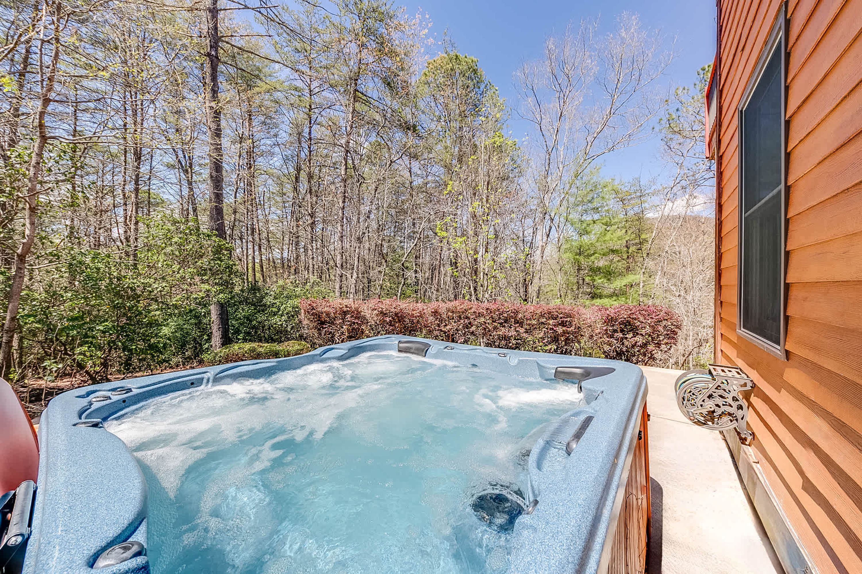 A hot tub in a backyard with a wooden house and trees in the background.