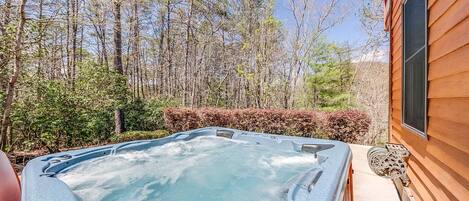 A hot tub in a backyard with a wooden house and trees in the background.