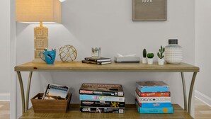 Ein Holztisch mit einer Lampe, Büchern, einer Taschentuchbox und kleinen Pflanzen.