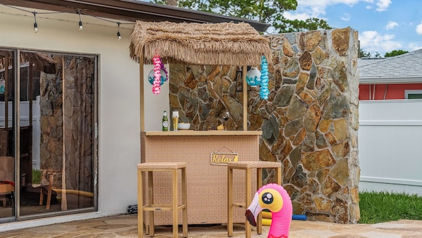 A tiki bar with a stone wall backdrop, a pool with a pink flamingo float, and a sign that reads 'Relax'. - Waterfront Retreat w Heated Pool Fire (Seminole)