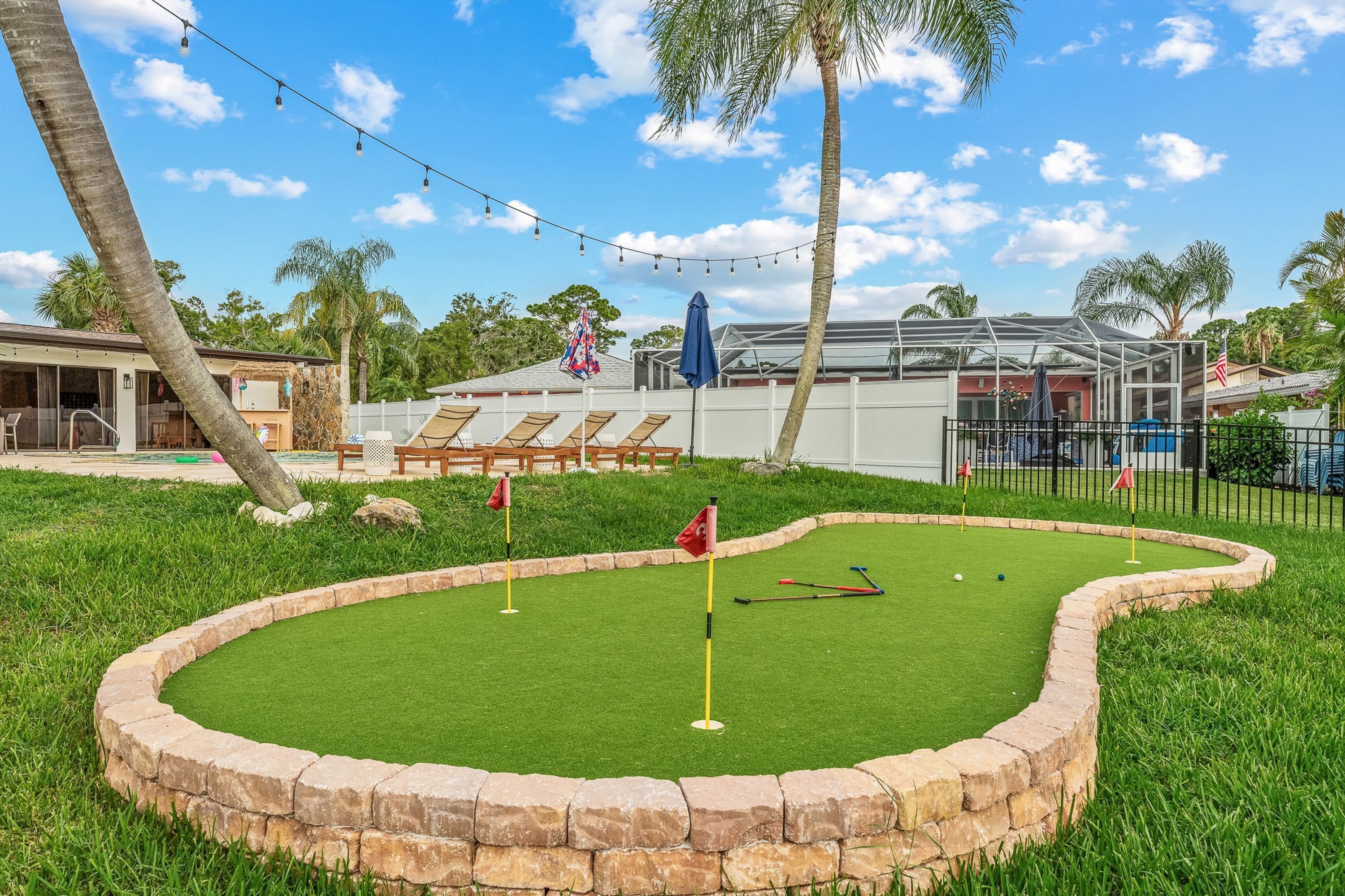 A miniature golf course with a stone border, a flag, and a golf club.
