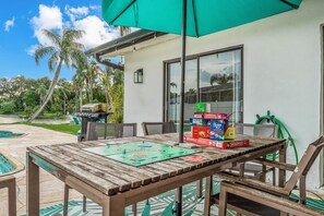 Un patio al aire libre con una mesa de madera, un juego de Monopoly y un paraguas verde.