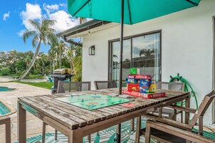 Un patio al aire libre con una mesa de madera, un juego de Monopoly y un paraguas verde.