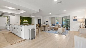 Una cocina moderna con una isla central, una zona de comedor con un sofá y una mesa baja, y una sala de estar con un ventanal grande.