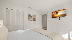 Un dormitorio con cama, armario, puerta y televisor de pared.
