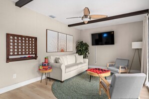 Ein Wohnzimmer mit einer Couch, einem Couchtisch, einem Fernseher, einem Deckenventilator und einer Pflanze.