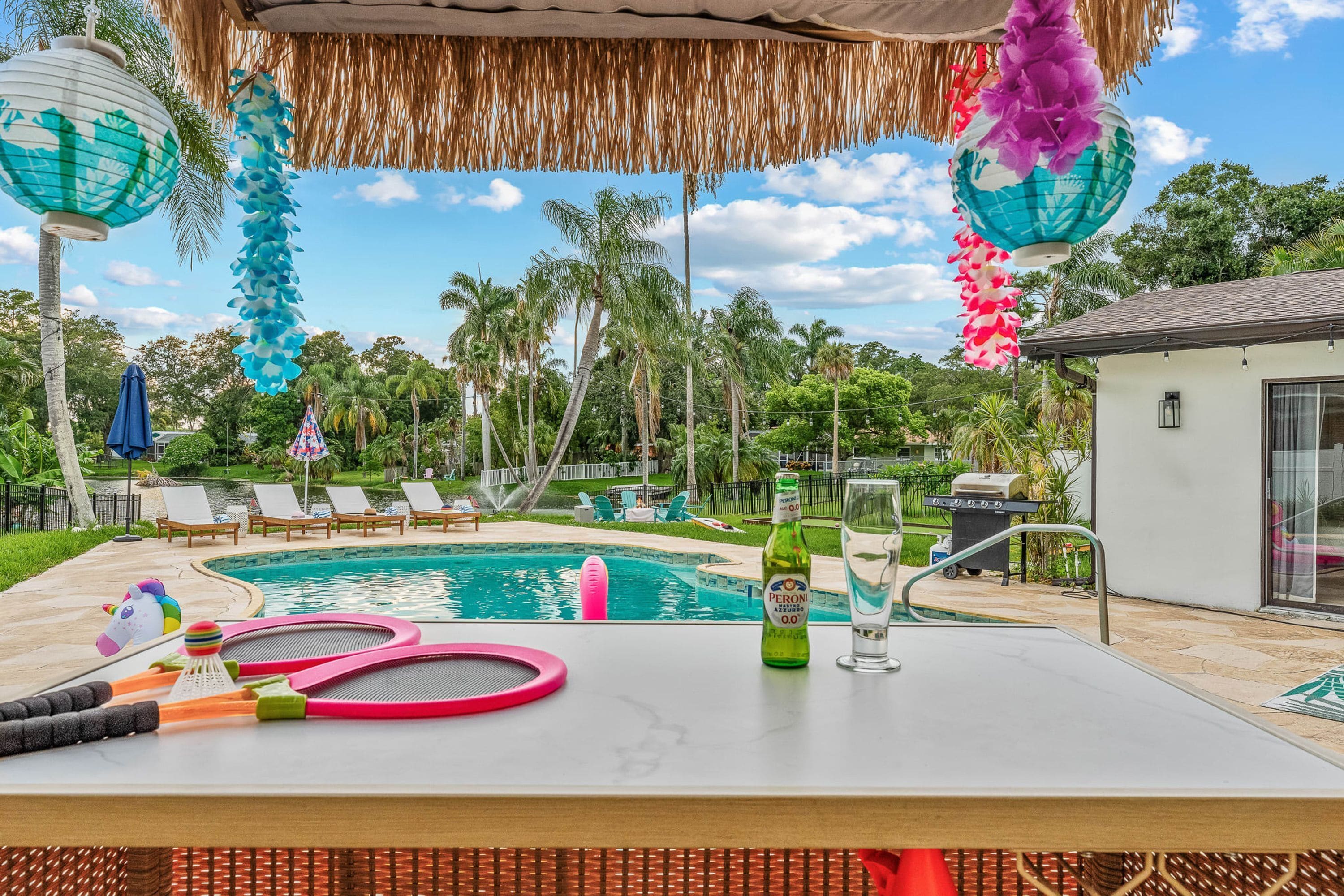 A poolside area with lounge chairs, a table with a bottle and glass, and a tiki-style umbrella.