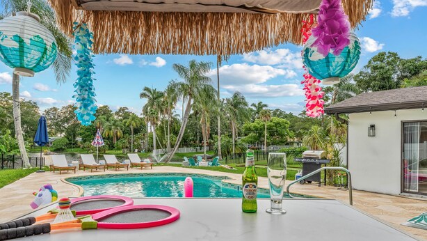 Un área de piscina con sillas de descanso, una mesa con una botella y un vaso, y un paraguas de estilo tiki.