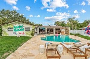 Ein Garten mit Swimmingpool, Liegestühlen und einem Haus mit Wandgemälde im tropischen Stil.