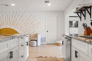 Una cocina moderna con armarios blancos, encimera de mármol y un original diseño de pared en forma de sol.