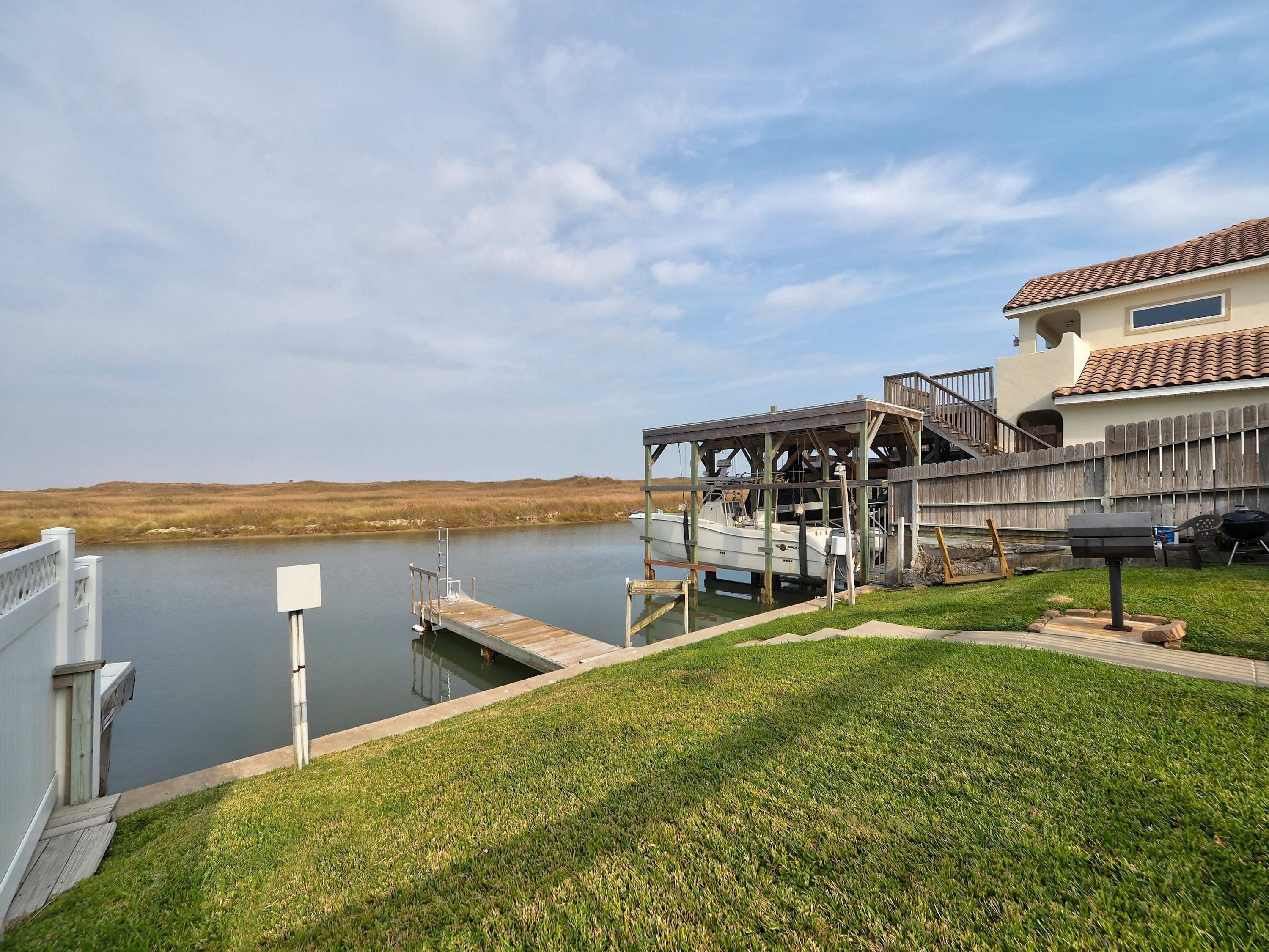 A waterfront property with a dock, a covered boat launch, and a house with a tiled roof.