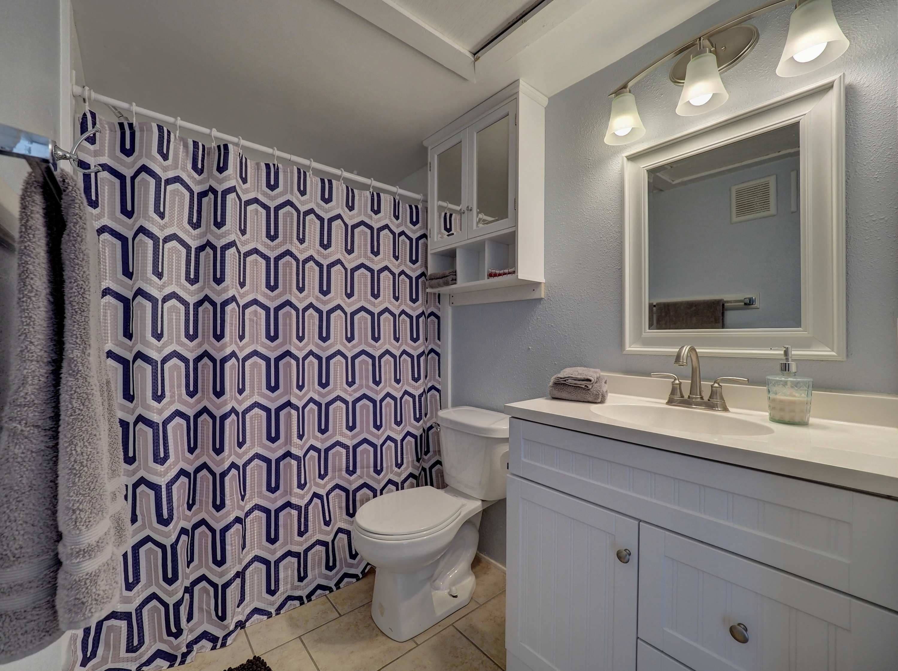A bathroom with a patterned shower curtain, a toilet, a sink with a mirror, and a cabinet.