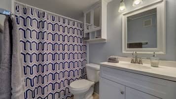 A bathroom with a patterned shower curtain, a toilet, a sink with a mirror, and a cabinet.