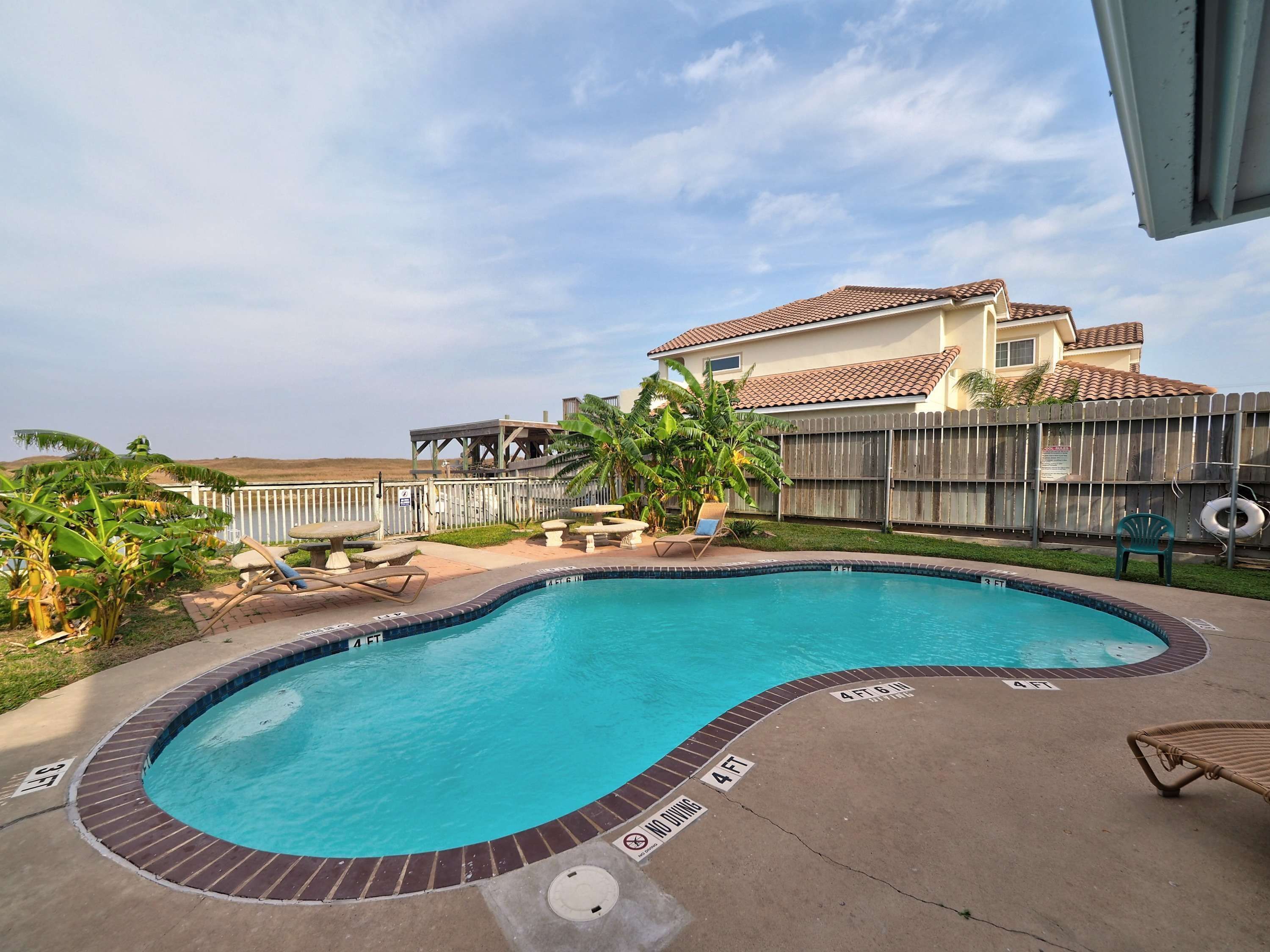 A swimming pool with a curved edge, surrounded by a concrete deck and a wooden fence.