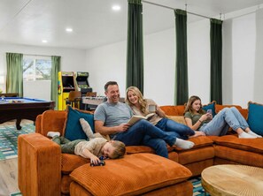 Eine Familie in einem Wohnzimmer mit Billardtisch, Kicker und einer Couch.