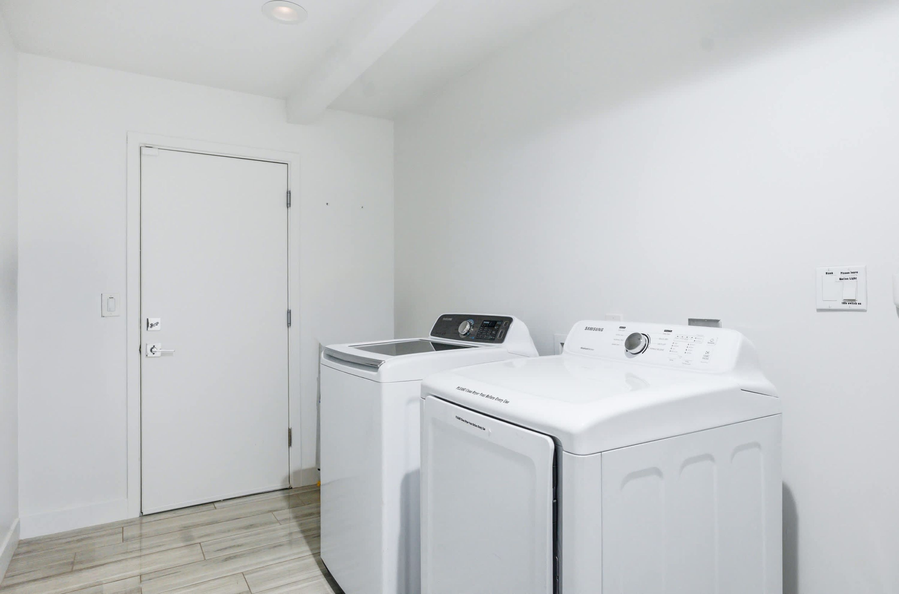 A laundry room with a white door, two white washing machines, and a wall-mounted control panel.
