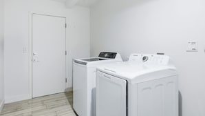 A laundry room with a white door, two white washing machines, and a wall-mounted control panel. - Fun-filled Oasis Pool Pickleball Games Galore (Scottsdale)