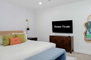 Ein Schlafzimmer mit einem Bett, einem an der Wand montierten Fernseher und einem Nachttisch.
