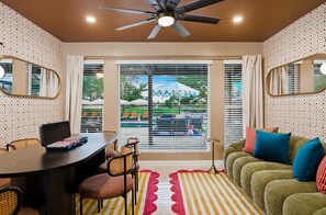 A room with a ceiling fan, a dining table with chairs, a sofa with cushions, and a window with blinds. - Fun-filled Oasis Pool Pickleball Games Galore (Scottsdale)