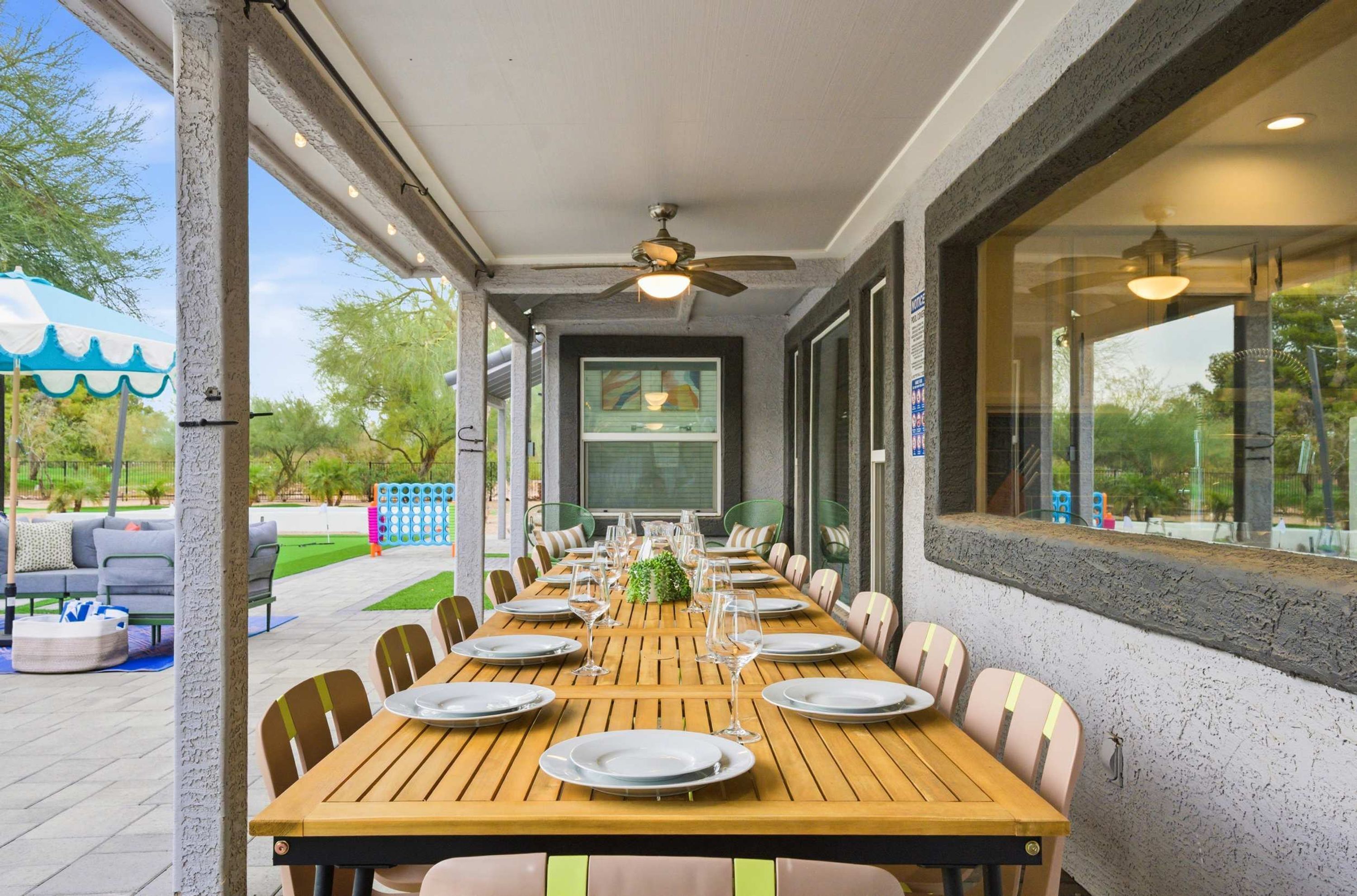 An outdoor dining area with a long wooden table set for a meal, surrounded by chairs.