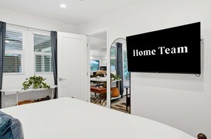 A bedroom with a bed, a TV mounted on the wall, and a view into the adjacent room. - Fun-filled Oasis Pool Pickleball Games Galore (Scottsdale)