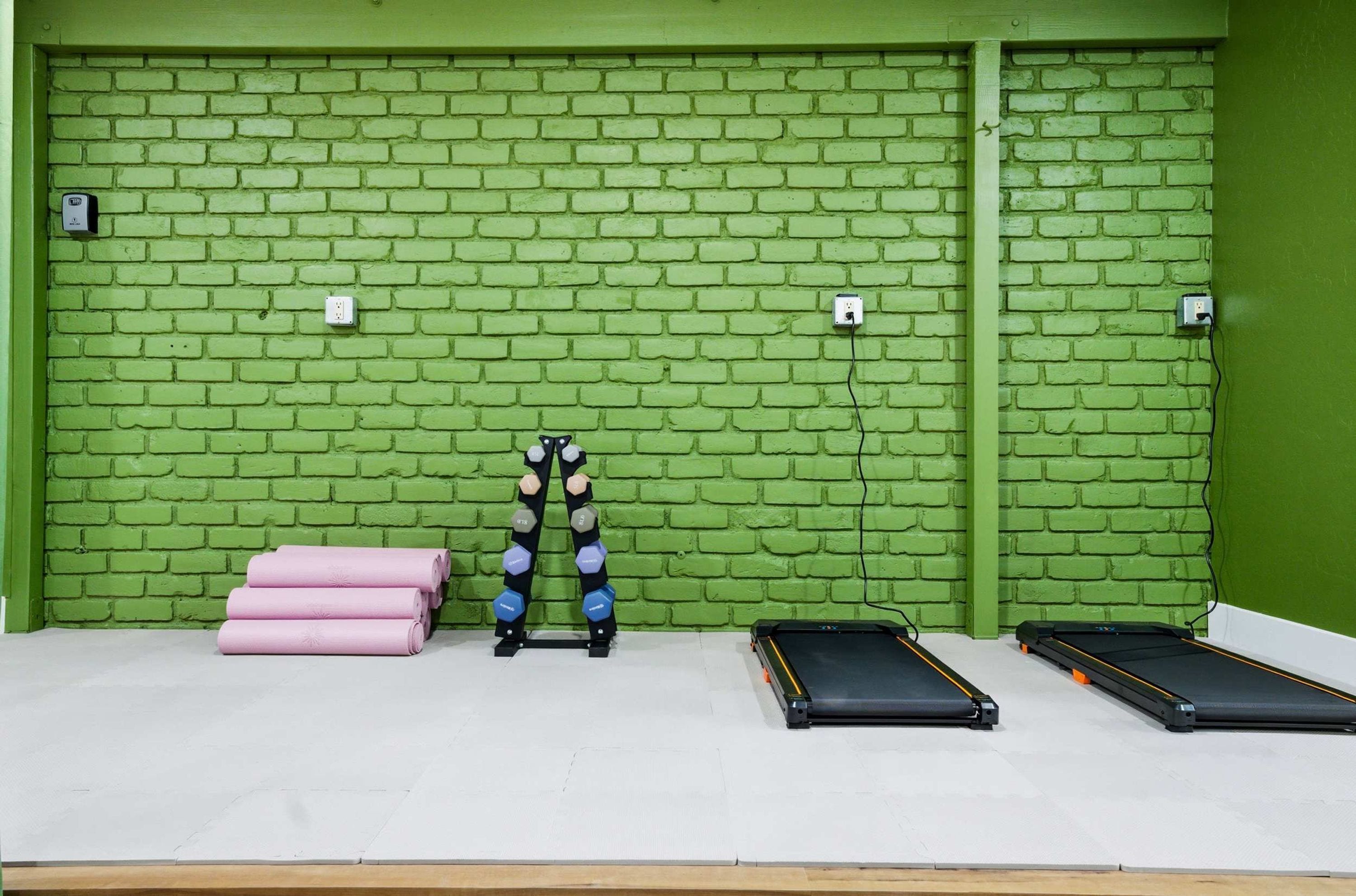 A gym with exercise equipment against a green brick wall.