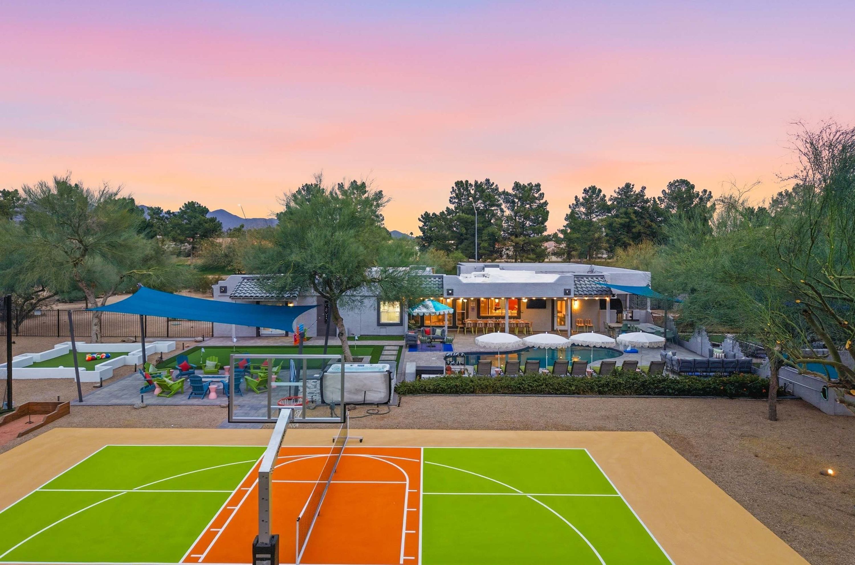 A tennis court with a net, a pool area with lounge chairs, and a building with outdoor seating.