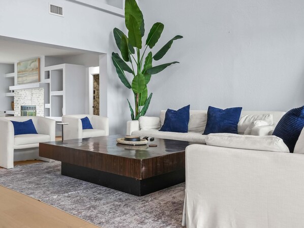 Una sala de estar moderna con una planta grande, sofás blancos y una mesa de centro.
