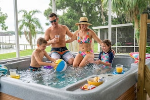 A family enjoying a hot tub with a view of a lake and palm trees. - Luxe Lakefront w Pool Pickleball Private Dock (Sebring)