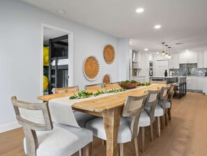 Un comedor moderno con una mesa y sillas de madera, una cocina al fondo y decoración en las paredes.