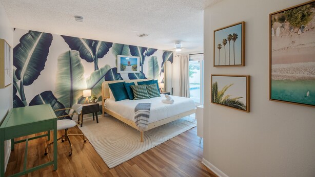 A bedroom with a bed, a desk, and a chair. There are wall art pieces and a large leaf pattern on the wall. - Epic Yard Movie Theater Pool Arcade Games (Seminole)