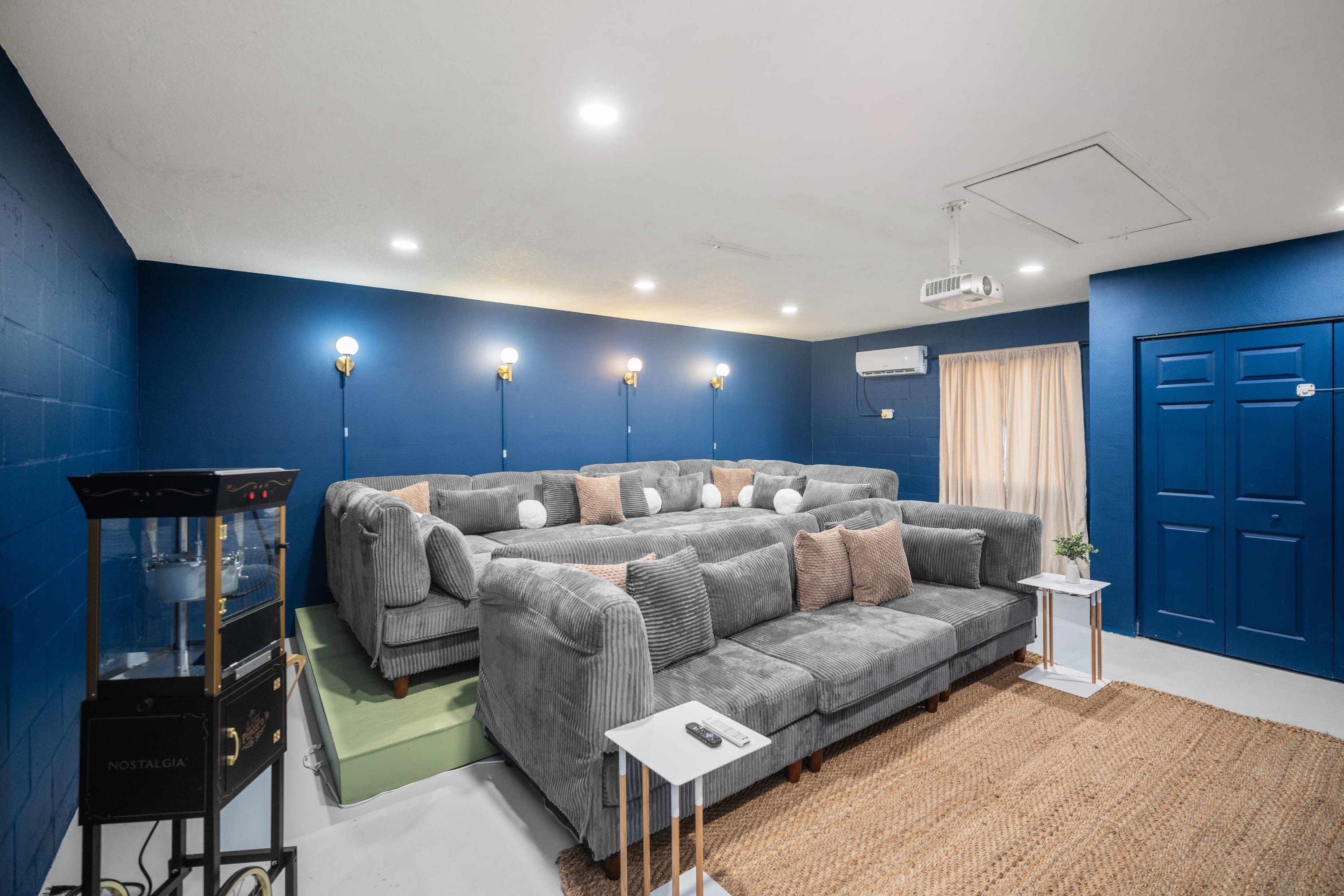 Una sala de estar moderna con un sofá seccional, una mesita auxiliar, un proyector y una pared azul.